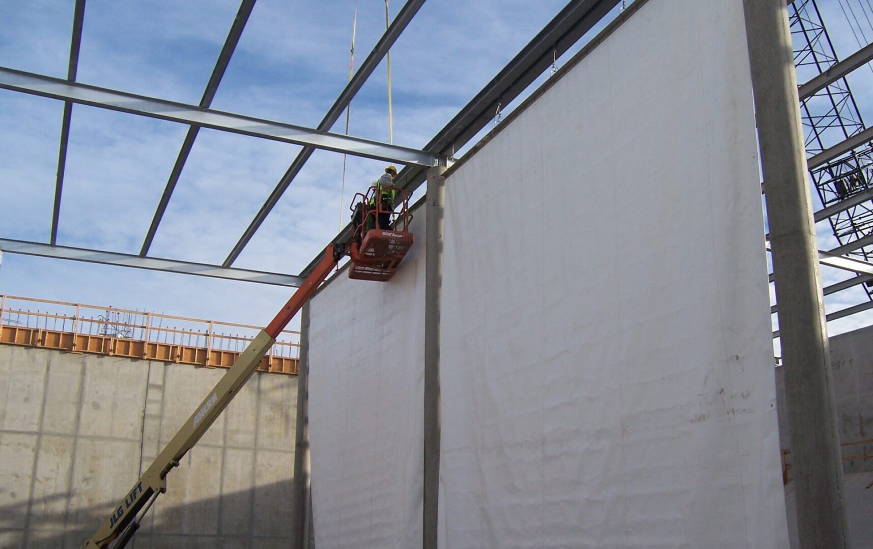 A man on a crane painting the side of a building.