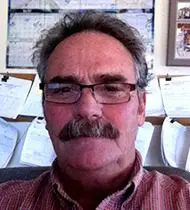 A man with glasses and mustache in front of papers.